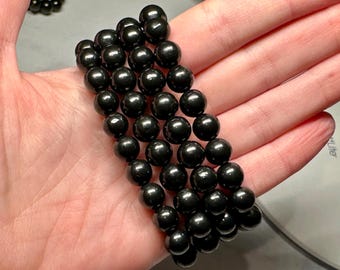 May include: A set of four black beaded bracelets, each with round beads, stacked on top of each other on a person's hand.