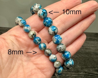 May include: Two beaded bracelets made of round, polished stones with a mottled pattern of bright blue, white, and dark gray. One bracelet features beads measuring 10mm in diameter, while the other bracelet consists of smaller 8mm beads.