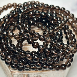 Peut inclure: Plusieurs bracelets compos&eacute;s de perles rondes, translucides et brun fonc&eacute;. Les perles sont enfil&eacute;es, formant plusieurs brins. Les bracelets sont empil&eacute;s, cr&eacute;ant un effet de superposition. Les perles ont un aspect poli et brillant. Chaque perle mesure environ 0,8 cm de diam&egrave;tre.