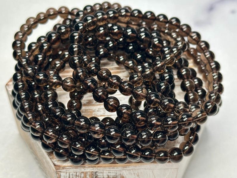 Peut inclure: Plusieurs bracelets compos&eacute;s de perles rondes, translucides et brun fonc&eacute;. Les perles sont enfil&eacute;es, formant plusieurs brins. Les bracelets sont empil&eacute;s, cr&eacute;ant un effet de superposition. Les perles ont un aspect poli et brillant. Chaque perle mesure environ 0,8 cm de diam&egrave;tre.