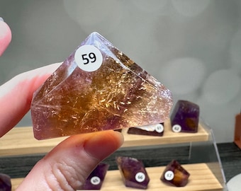 May include: A triangular-cut gemstone featuring a gradient of translucent amber and deep purple hues. The crystal has a polished surface with internal fractures and a white circular sticker labeled with the number 59 on the front face.