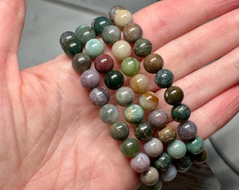 Puede incluir: Un conjunto de cuatro pulseras hechas con cuentas de ágata multicolores. Las cuentas son redondas y tienen un aspecto moteado, con tonos de verde, marrón, rojo y blanco.