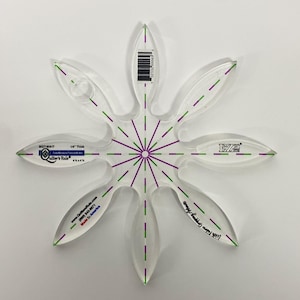 May include: Clear acrylic quilting template in a flower shape. The template has green and purple markings and the text "Quilter's Rule". The template is 1/4" thick and has a barcode. The template is designed for quilting.