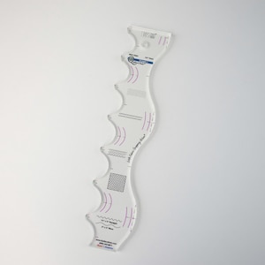 May include: A clear, curved quilting ruler with a wavy edge and various markings. The ruler features purple and black printed designs, including curved lines, zigzags, and a grid pattern. Text on the ruler includes measurements and the name of the manufacturer.