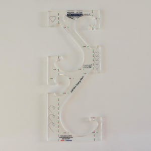 May include: A clear plastic quilting template with a heart design and instructions for use. The template is marked with measurements in inches and includes the text "Little  Trims  Company  Studio".
