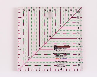May include: A clear plastic quilting ruler with a 1/8 inch thickness. The ruler has a grid pattern with red and green lines. The ruler is labeled "Quilter's Rule" and has a website and phone number printed on it. The ruler is made in America.