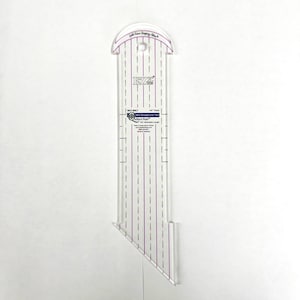 May include: A clear acrylic quilting ruler with purple markings and the text "EZ Quilting". The ruler has a curved top with a hole for hanging and a pointed bottom. It is designed for straight line quilting and measures 4.5 inches in length.
