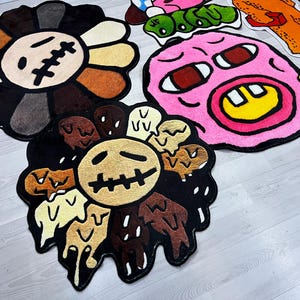 May include: A set of five colorful, cartoon-style rugs. The rugs feature a flower, a face with a big smile, and a face with a frown. The rugs are made of a soft, plush material.