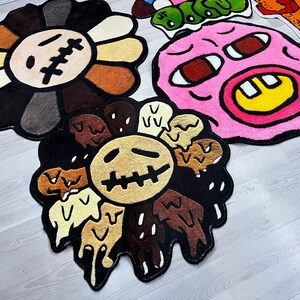 May include: Three colorful, cartoon-style rugs with different designs. The first rug is a black and brown flower with a yellow center and a stitched-up mouth. The second rug is a pink face with a yellow smile and red eyes. The third rug is a black and brown flower with a yellow center and a stitched-up mouth.