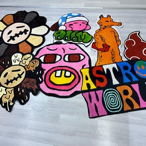 May include: A set of colorful, cartoon-style rugs featuring various characters and designs. The rugs include a pink face with a yellow smile, a brown flower with a face, a brown cloud, a yellow and orange character, and a multi-colored rug with the text "ASTRO WORLD".
