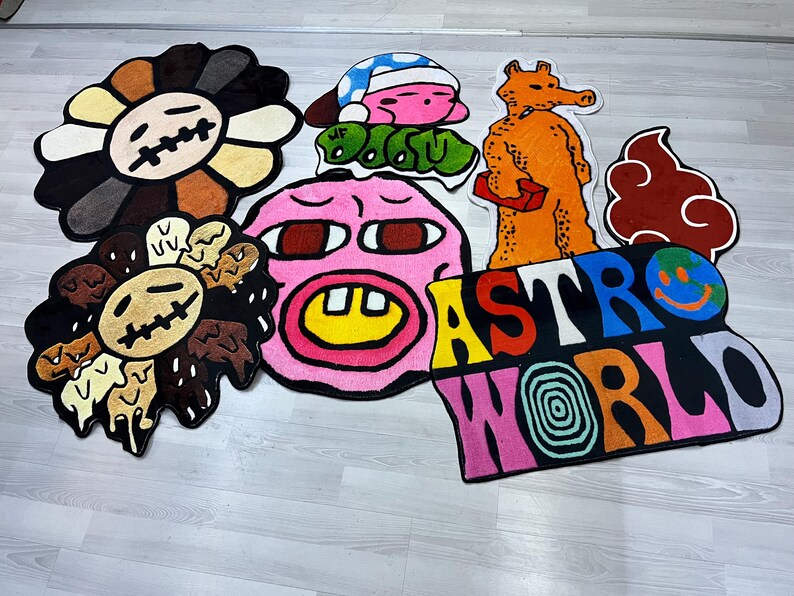 May include: A set of colorful, cartoon-style rugs featuring various characters and designs. The rugs include a pink face with a yellow smile, a brown flower with a face, a brown cloud, a yellow and orange character, and a multi-colored rug with the text "ASTRO WORLD".