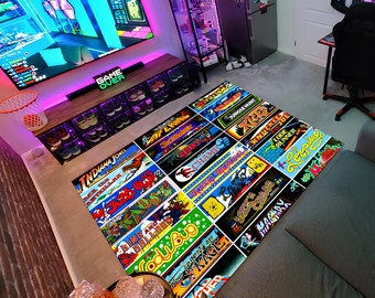 Puede incluir: Una alfombra colorida con un tema de juegos de arcade retro. La alfombra presenta los nombres de juegos de arcade clásicos como Indiana Jones, Jungle Hunt y King of Fighters.