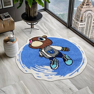 May include: A blue and white round rug with a cartoon bear wearing a grey jacket and a blue and white hat. The bear is floating in the air and the rug has a white border.