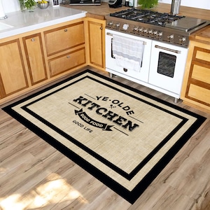 Puede incluir: Alfombra de cocina rectangular con textura tejida beige y borde negro. La alfombra presenta el texto "YE OLDE KITCHEN GOOD FOOD GOOD LIFE" en un estilo vintage. La alfombra está colocada sobre un suelo de madera frente a una cocina.