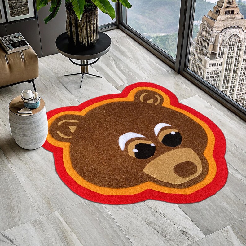 May include: A brown bear face rug with orange and red trim. The rug is made of plush, fuzzy material.