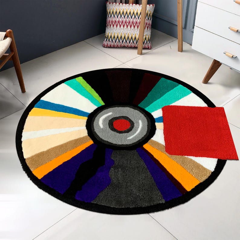 May include: A round, colorful rug with a black and white record design in the center. The rug has a variety of colors, including red, orange, yellow, green, blue, and purple. The record design has a red center and a gray outer ring.