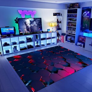 May include: A gaming room featuring a large TV, consoles, and a patterned rug. The rug has a hexagonal design with red and blue hues. Shelving units display games and accessories, illuminated by blue and green lighting.