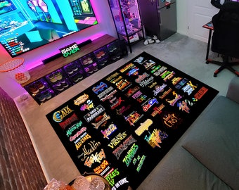 Puede incluir: Una alfombra negra con una variedad de logotipos de videojuegos coloridos impresos en ella. Los logotipos incluyen títulos como "Super Mario All-Stars", "Aladdin", "Zombies Ate My Neighbors" y "Lufia".