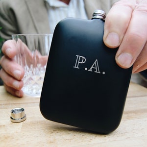 May include: Black metal hip flask with a silver cap and the initials "P.A." engraved on the front.