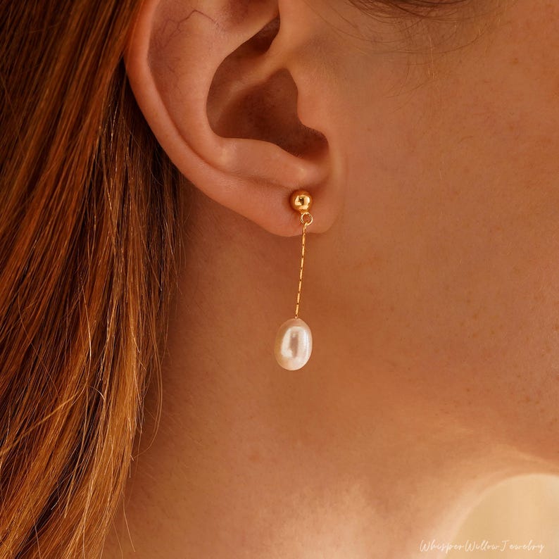 May include: A gold chain earring with a single white pearl dangling from it.