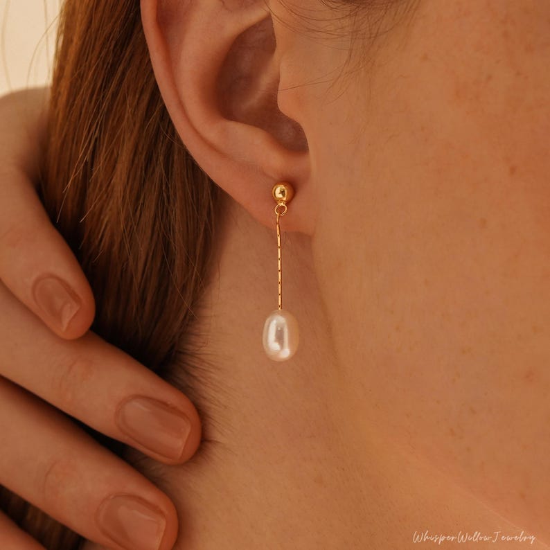 May include: Gold dangle earrings with a single white pearl hanging from a delicate chain.