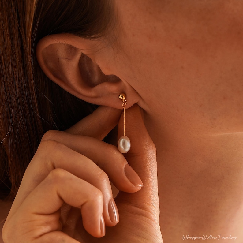 May include: A single gold earring with a delicate chain and a white pearl drop.