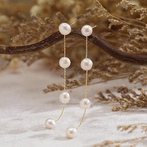 May include: Dangle earrings with white pearls suspended from fine gold chains. The earrings have a cascading design with multiple pearls of different sizes, creating a graceful look. These earrings are ideal for adding a touch of classic beauty to any outfit.