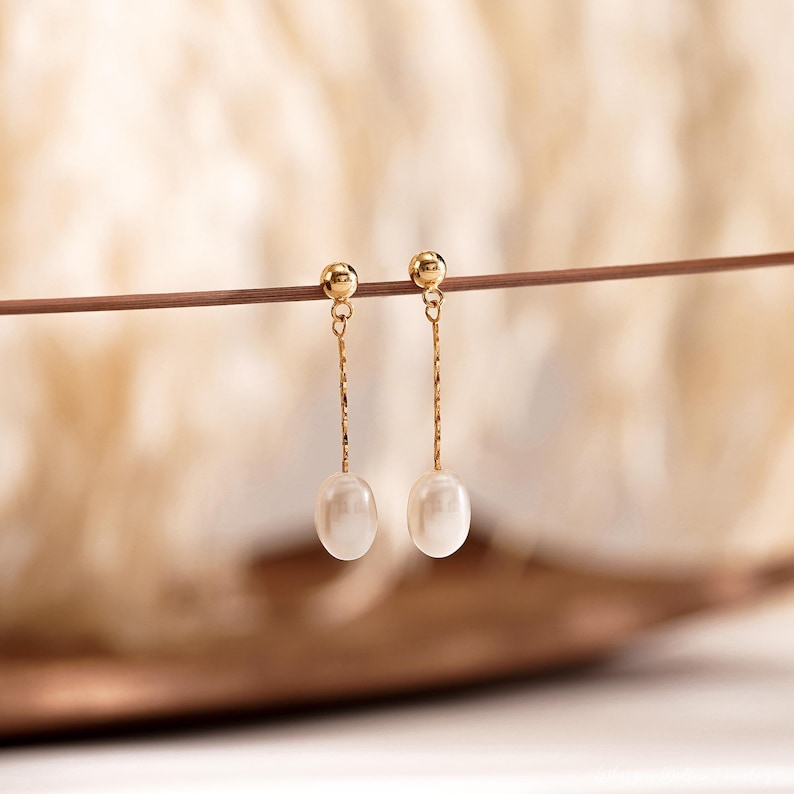 May include: A pair of gold drop earrings with a single white pearl on each earring.