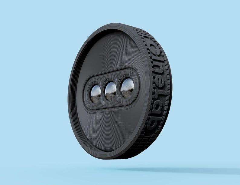 May include: A black, circular device with three reflective lenses and the text "oneLab" embossed on the side. The device has a textured edge and a series of concentric circles on its face. The background is a solid light blue.