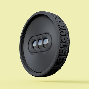 May include: A black, circular device with the text "oneLab" embossed on the side. The device has a textured edge and a recessed section with three circular lenses. The background is a pale yellow.