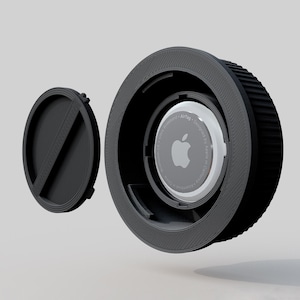 Könnte beinhalten: Ein schwarzer, kreisförmiger AirTag-Halter mit geriffeltem Außenring und separatem, kleinerem Deckel. Der Apple AirTag ist im Halter sichtbar. Das Design ist modern und funktional, wahrscheinlich 3D-gedruckt.