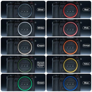 May include: A collection of black Lumix S5 cameras, each featuring a different colored accent ring around the lens: silver, red, white, pink, cream, orange, forest green, yellow, green, and blue. Each camera has the Lumix logo.