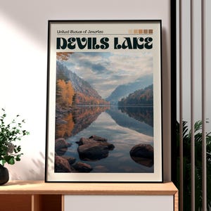 May include: A framed art print depicting Devils Lake in the United States of America. The image shows a tranquil lake scene with mountains and autumnal trees reflected in the water. The title "Devils Lake" is written in a bold, decorative font.