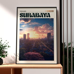 May include: Framed art print featuring a cityscape of Surabaya, Indonesia, under a vibrant sunset sky. The word "SURABAYA" is displayed in bold, stylized font above the image. The print is in a black frame.