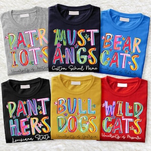 May include: Six different t-shirts with colorful, cartoon-style text. The shirts feature the names of different college teams, including the University of Kentucky, University of Florida, Louisiana State University, University of Georgia, and University of Missouri. The shirts are all in different colors, including gray, blue, black, yellow, and red.