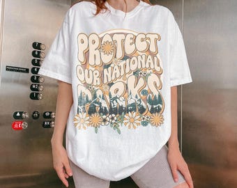 May include: White t-shirt with a retro-style graphic that says "Protect Our National Parks" with a mountain and flower design.