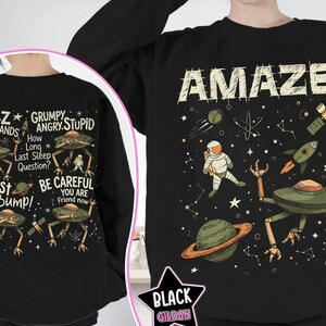 May include: Black sweatshirt with a space-themed graphic. The front features the word "AMAZE!" with an astronaut, planets, and a rocket. The back displays alien-like creatures and phrases like "Jazz Hands" and "Fist My Bump!"