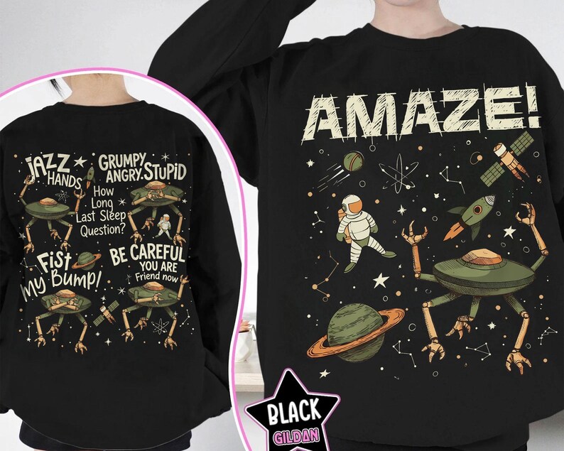 May include: Black sweatshirt with a space-themed graphic. The front features the word "AMAZE!" with an astronaut, planets, and a rocket. The back displays alien-like creatures and phrases like "Jazz Hands" and "Fist My Bump!"