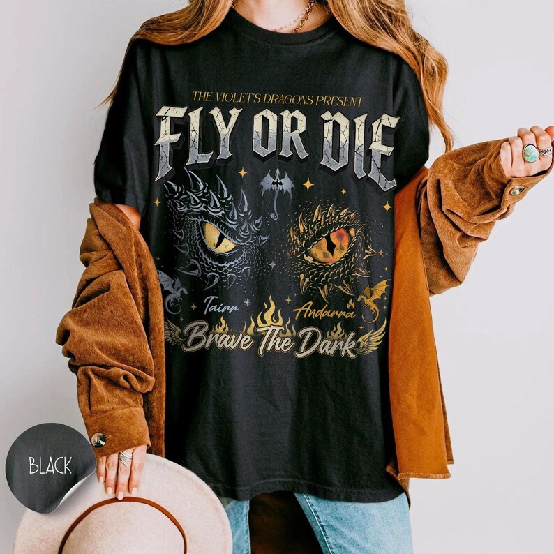 May include: Black t-shirt with a graphic design featuring dragon eyes and the text "FLY OR DIE". The design includes the words "Tainn" and "Andarra", and the phrase "Brave The Dark". The shirt is a classic crew neck.