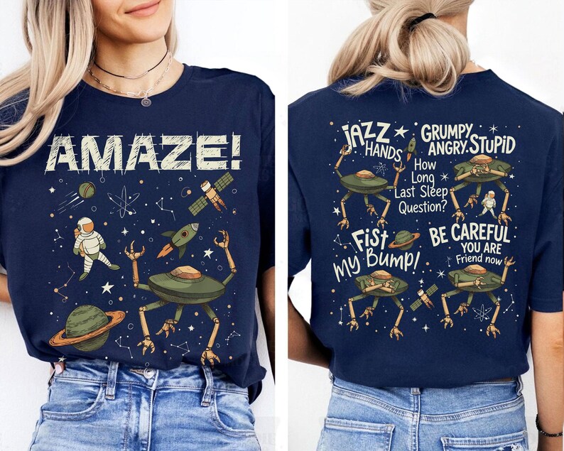 May include: Navy blue t-shirt with a space-themed graphic. The front features the word "AMAZE!" with an astronaut, planets, and rockets. The back displays alien figures and phrases like "JAZZ HANDS" and "BE CAREFUL".