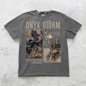 May include: A dark gray t-shirt with a graphic print of a dragon, a castle, and a book. The text "ONYX STORM" is printed in large letters at the top of the shirt. The text "BASGIATH WAR + COLLEGE" is printed at the bottom of the shirt. The text "I WILL NOT DIE TODAY I WILL SAVE HIM" is printed on the book.