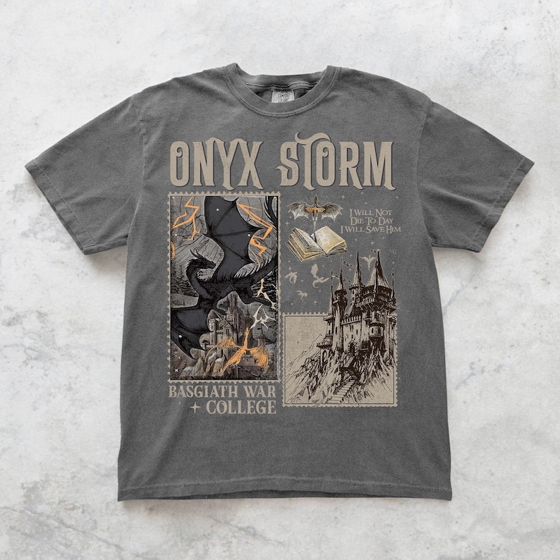 May include: A dark gray t-shirt with a graphic print of a dragon, a castle, and a book. The text "ONYX STORM" is printed in large letters at the top of the shirt. The text "BASGIATH WAR + COLLEGE" is printed at the bottom of the shirt. The text "I WILL NOT DIE TODAY I WILL SAVE HIM" is printed on the book.
