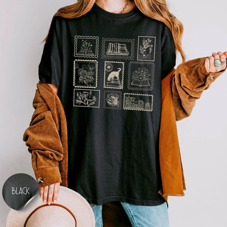 Puede incluir: Camiseta negra con dise&ntilde;os de sellos postales beige que representan libros, flores y un gato. La camiseta tiene un estilo casual. Las ilustraciones son de estilo vintage.