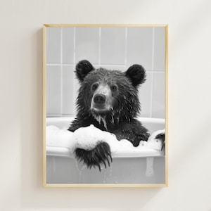 May include: A black and white photo of a bear taking a bath in a white bathtub. The bear is covered in bubbles and has a surprised expression on its face.