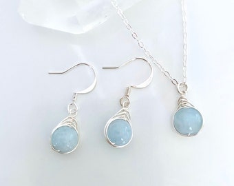May include: A set of aquamarine gemstone jewelry featuring a necklace and earrings. The stones are wrapped in silver wire and hang from delicate silver chains.