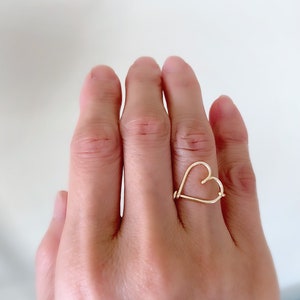 May include: A gold heart-shaped ring worn on a finger.