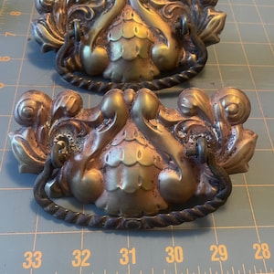 Puede incluir: Dos tiradores de cajón antiguos de latón con diseños florales ornamentados. Los tiradores tienen un acabado dorado con detalles más oscuros y un asa trenzada en forma de cuerda. Adecuado para la restauración de muebles.