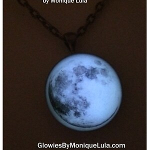 Puede incluir: Un collar con cadena plateada y un colgante redondo con una imagen en blanco y negro de la luna. El colgante brilla en la oscuridad. Hecho a mano en California por Monique Lula. GlowiesByMoniqueLula.com