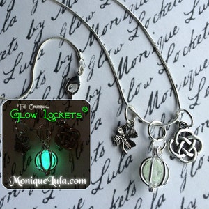 May include: A silver chain necklace with four charms: a shamrock, a Celtic knot, a feather, and a glowing green glass locket. The locket is labeled "The Original Glow Lockets" and "Monique Lula.com".