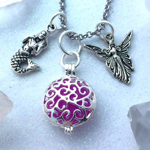 May include: A silver chain necklace with a pink and silver charm, a silver mermaid charm, and a silver fairy charm. The necklace is on a white background.